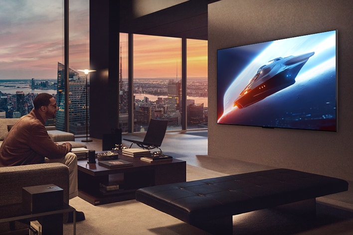 Sala de estar elegante en un penthouse. Hermoso paisaje urbano visible desde la ventana. Un hombre sentado en el sofá viendo contenido en una TV Wall Mounted.