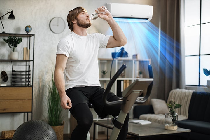 Este es un video del aire que sale de un aire acondicionado detrás de un hombre sentado en una máquina de ejercicios mientras bebe agua.