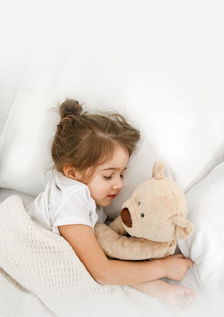 Una niña está acostada en la cama con un peluche en los brazos.