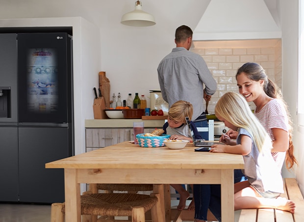 Toda la familia está sentada a la mesa preparando una comida. El refrigerador InstaView instalado en un lado de la cocina genera aire frío rápidamente.