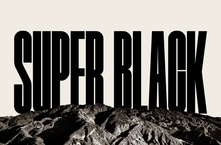 Las palabras "SUPER BLACK" aparecen en mayúsculas negras en negrita. Una escena montañosa negra con una definición nítida se eleva para cubrir las letras, revelando también un pueblo y dunas de arena. La copia negra desaparece detrás de un cielo negro.