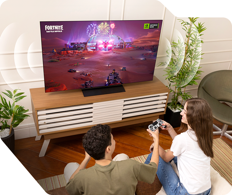 Vista aérea de la sala de estar. Bruno y su novia jugando FORTNITE, con efectos de sonido saliendo de la TV LG OLED C4.