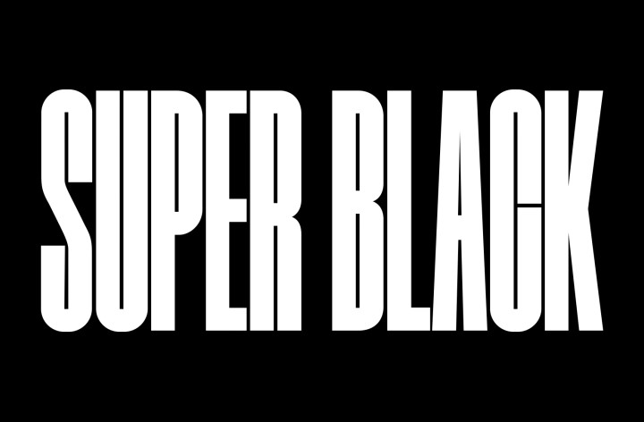 Las palabras "SUPER BLACK" aparecen en mayúsculas negras en negrita. Una escena montañosa negra con una definición nítida se eleva para cubrir las letras, revelando también un pueblo y dunas de arena. La copia negra desaparece detrás de un cielo negro.