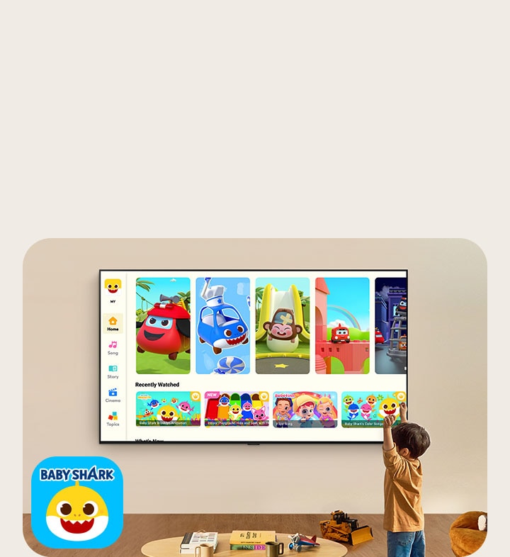 Malý chlapec sleduje platformu Pinkfong na televizoru LG připevněném na zdi v obývacím pokoji s dětskými hračkami. 