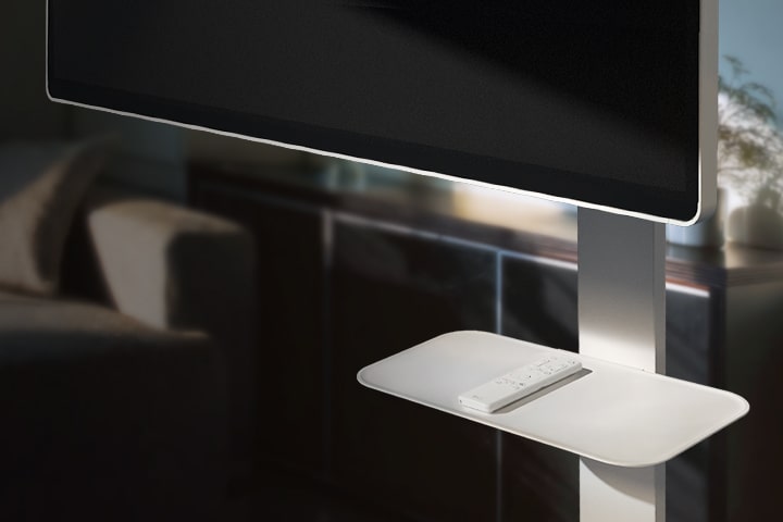 Otočný stojan na TV s připevněnou otočnou deskou pro dálkové ovládání, umístěný v moderním obývacím pokoji.