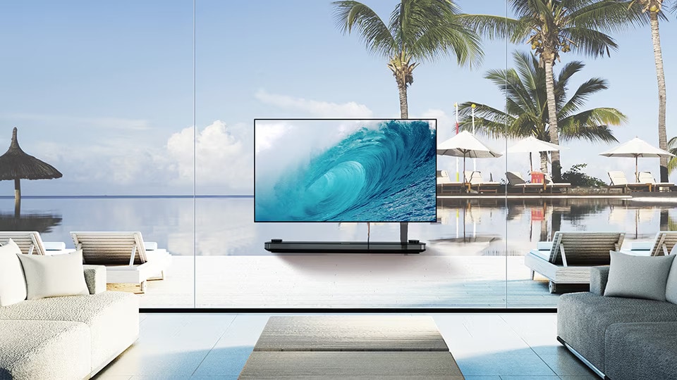 Televize LG SIGNATURE OLED TV W zobrazuje chladnou vlnu na obrazovce, zatímco je položena v obývacím pokoji s modrým výhledem na oceán za oknem.