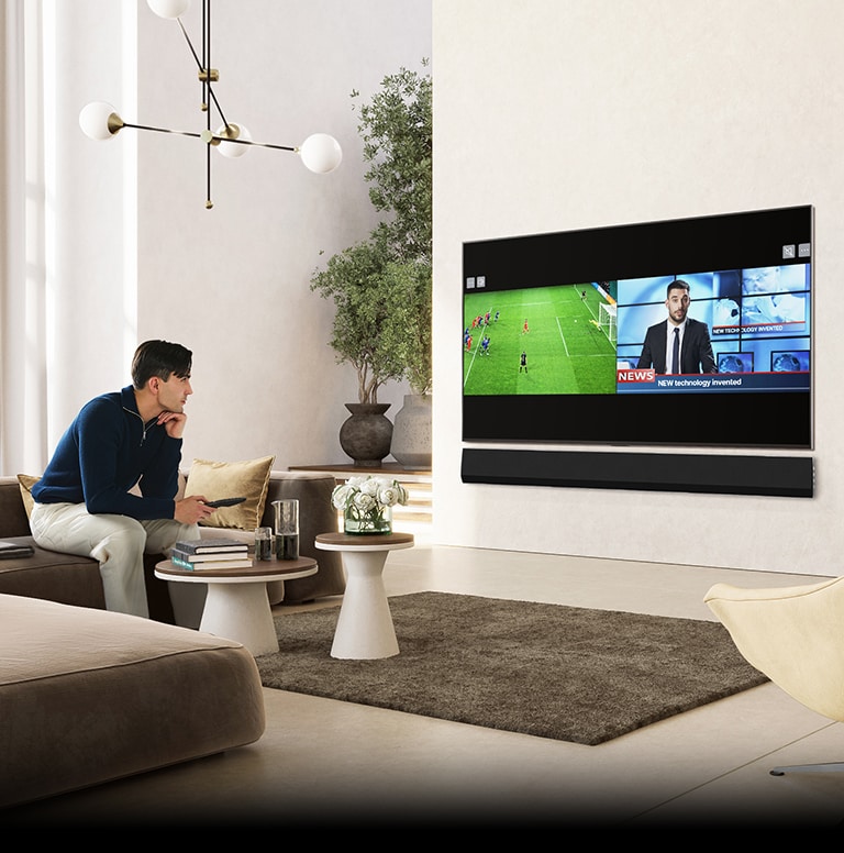 Muž sedí na luxusní a prostorné pohovce v obývacím pokoji a sleduje televizor. Televizní obrazovka se rozdělí, přičemž na jedné straně se objeví fotbalový zápas a na druhé zpravodajství.