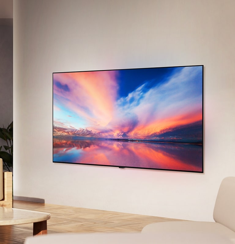 LG OLED TV, OLED B4 na stěně neutrálního obývacího prostoru zobrazující barevnou fotografii západu slunce nad oceánem.
