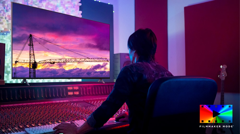 Filmový režisér se dívá na velký televizní monitor a něco upravuje. Na televizní obrazovce je vidět věžový jeřáb na fialové obloze. V pravém dolním rohu je umístěno logo FILMMAKER Mode.
