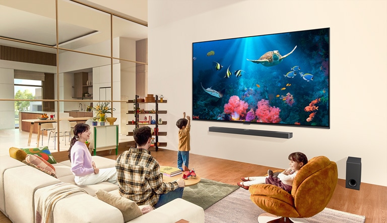 Rodina v obývacím pokoji s ultra velkým televizorem LG umístěným na stěně, na jehož obrazovce je výjev z oceánu včetně korálů a želvy.