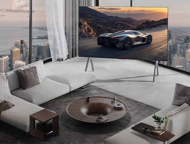 Geräumiges Wohnzimmer mit Blick auf eine Stadtlandschaft. Der LG OLED TV steht auf einem Standfuß. Das ultra-schlanke Design sorgt für eine beeindruckende Wirkung des Bildschirms. Die Zero Connect Box ist zu sehen, aber unauffällig aufgestellt.