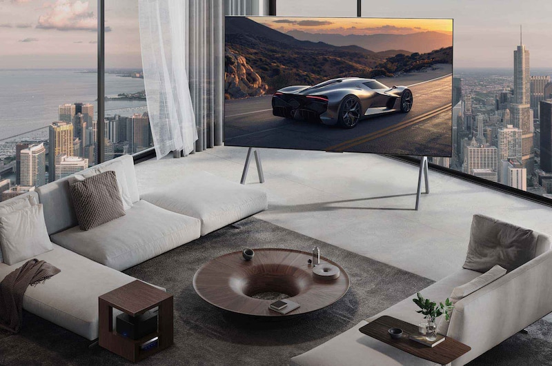 Geräumiges Wohnzimmer mit Blick auf eine Stadtlandschaft. Der LG OLED TV steht auf einem Standfuß. Das ultra-schlanke Design sorgt für eine beeindruckende Wirkung des Bildschirms. Die Zero Connect Box ist zu sehen, aber unauffällig aufgestellt.