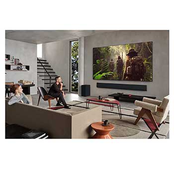 Wide view of a living room inside a premium home, a man is watching a movie on his wall-mounted LG OLED TV. The TV's design blends elegantly with the wall and the interior design.