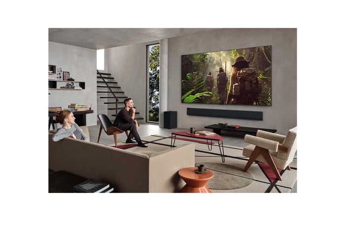 Weite Ansicht eines Wohnzimmers in einem hochwertigen Haus. Ein Mann sieht sich einen Film auf seinem an der Wand montierten LG OLED-Fernseher an. Das Design des Fernsehers fügt sich elegant in die Wand und die Inneneinrichtung ein.