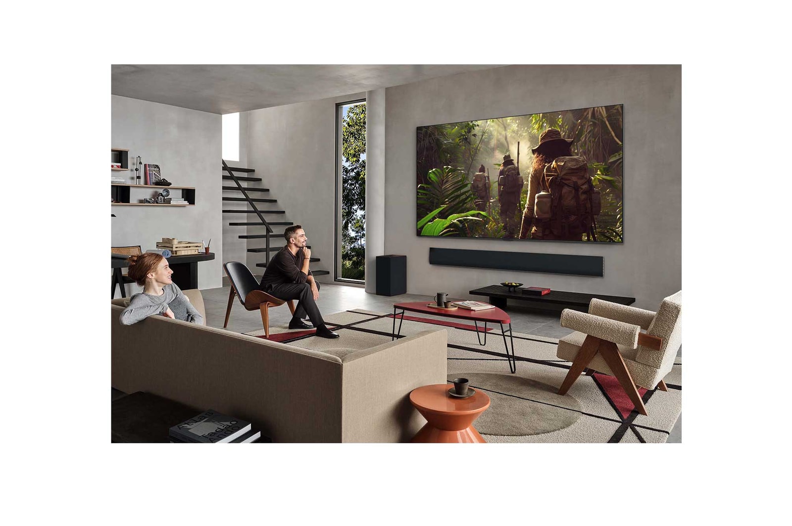 Weite Ansicht eines Wohnzimmers in einem hochwertigen Haus. Ein Mann sieht sich einen Film auf seinem an der Wand montierten LG OLED-Fernseher an. Das Design des Fernsehers fügt sich elegant in die Wand und die Inneneinrichtung ein.