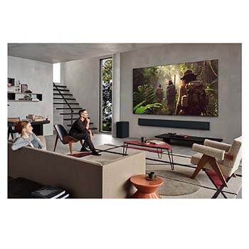 Weite Ansicht eines Wohnzimmers in einem hochwertigen Haus. Ein Mann sieht sich einen Film auf seinem an der Wand montierten LG OLED-Fernseher an. Das Design des Fernsehers fügt sich elegant in die Wand und die Inneneinrichtung ein.