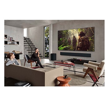 Wide view of a living room inside a premium home, a man is watching a movie on his wall-mounted LG OLED TV. The TV's design blends elegantly with the wall and the interior design.