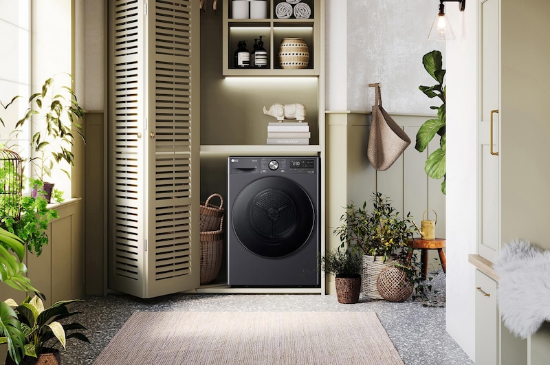 LG Trockner RT90V9B in Dunkelschwarz, elegant in einen hellgrünen Waschraum mit Holzakzenten und Pflanzen integriert.