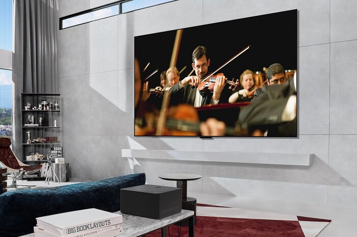 Zero Connect Box auf einem Tisch in einem luxuriösen Wohnzimmer streamt eine Orchesteraufführung auf den LG Signature OLED M4 True Wireless TV Fernseher.