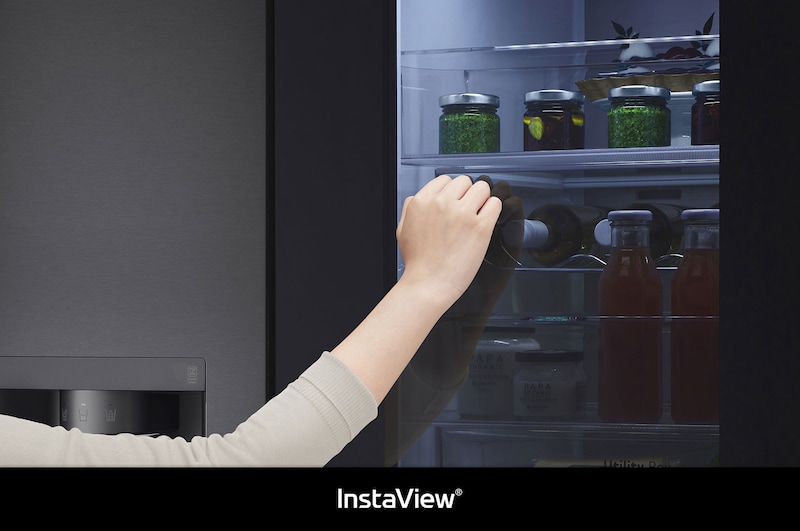 LG Side-by-Side GSXV91MCAE zeigt **InstaView** Door-in-Door: Eine Hand greift nach einer Flasche durch die halb geöffnete Innentür, wobei das beleuchtete Fach sichtbar ist.