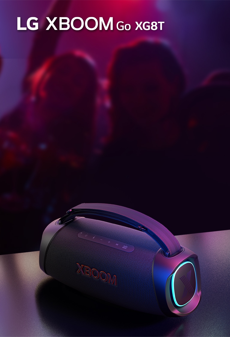 LG XBOOM Go DXG8T steht auf einem Metalltisch und das orange Licht ist eingeschaltet. Hinter dem Tisch genießen Menschen die Musik.