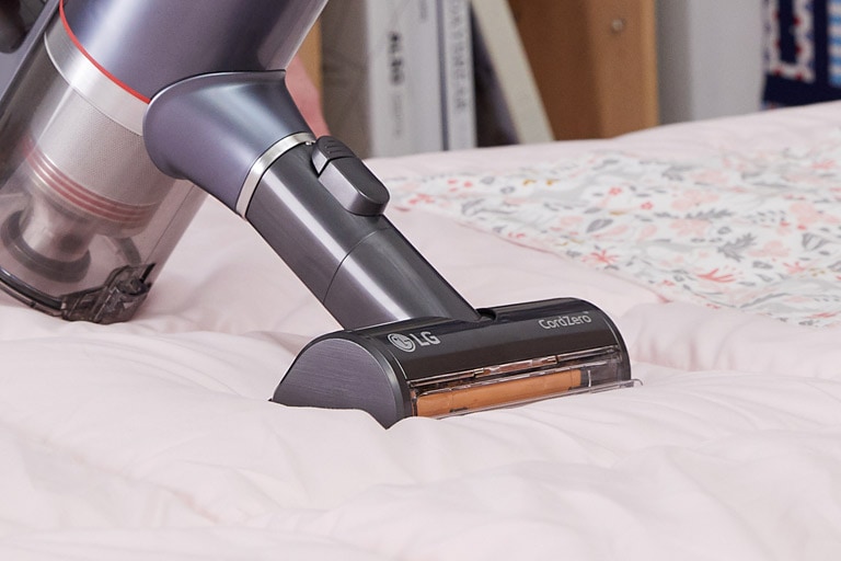 Die Power Punch-Düse für Polstermöbel wird mit dem Behälter gezeigt, der Schmutz und Staub von einem Bett entfernt.
