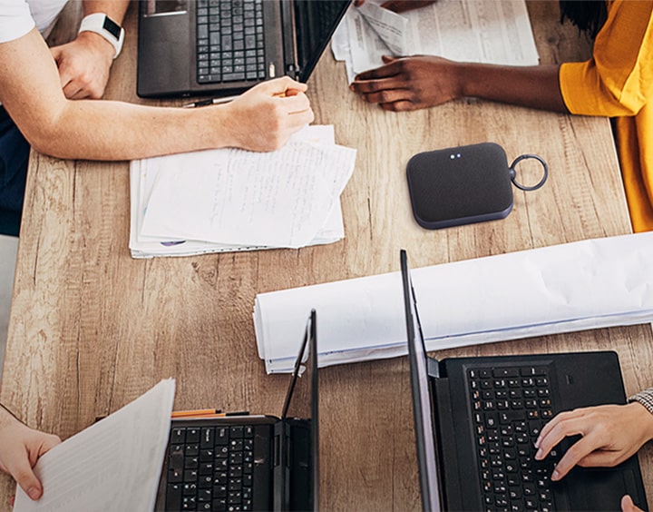 4 Personen arbeiten an einem Schreibtisch, jeder mit seinem eigenen Laptop. Gesichter sind nicht zu sehen, einige tippen, andere schreiben. Der XBOOM Go DXG1-Lautsprecher wird auf einem Schreibtisch aufgestellt.