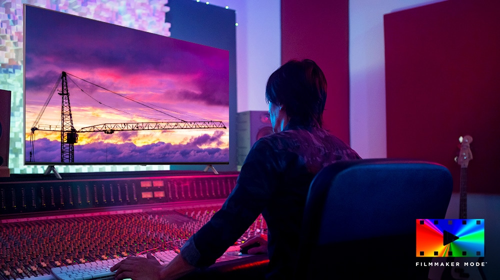 Ein Filmregisseur blickt auf einen großen TV-Monitor und bearbeitet etwas. Der Fernsehbildschirm zeigt einen Kran vor einem violetten Himmel. Das Logo des FILMMAKER MODE befindet sich in der unteren rechten Ecke.