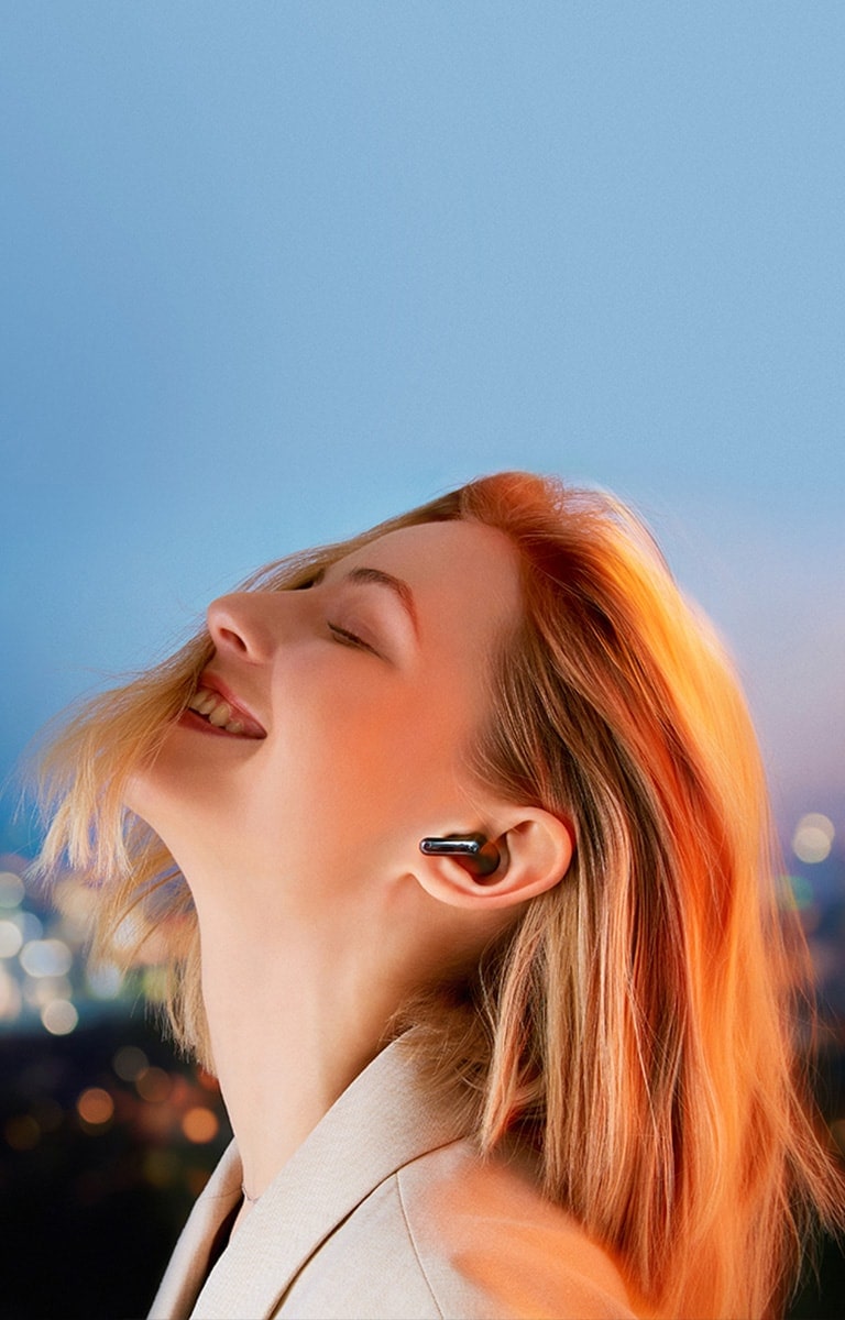 Hinter dem Satz „Glasklarer Hörgenuss“ erscheint eine Frau, die vor dem Hintergrund einer nächtlichen Stadtansicht über ihre TONE-Free-Earbuds in sich versunken der Musik lauscht.