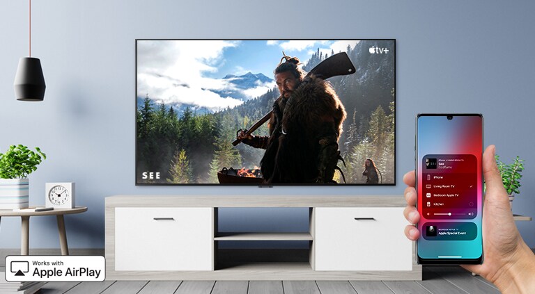 Nahaufnahme einer Hand, die den TV über ein iPhone steuert. Auf dem Fernseher werden Inhalte von Apple TV+ angezeigt.