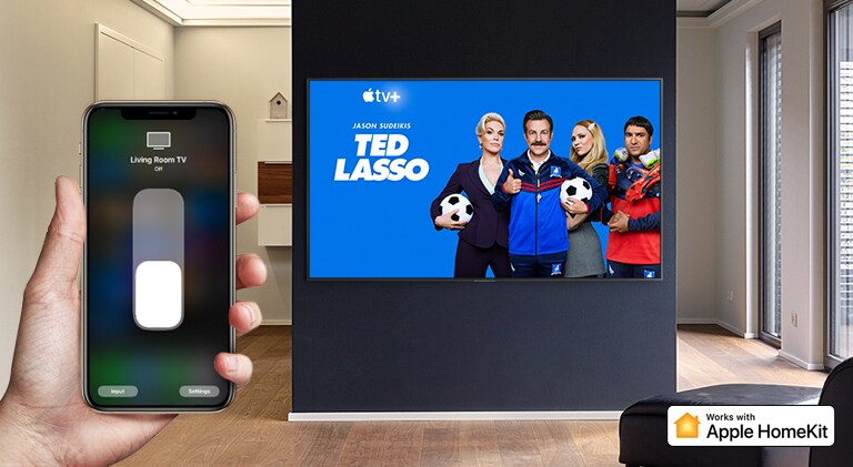 Nahaufnahme einer Hand, die den TV über ein iPhone steuert. Auf dem Fernseher werden Inhalte von Apple TV+ angezeigt, und zwar „Ted Lasso“.