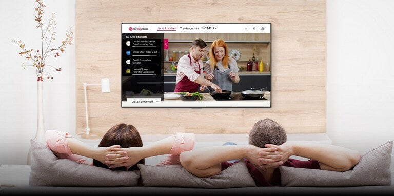 A man and woman are watching TV together. A cooking-related TV show is playing on the TV screen and the shop now button is popped up in the lower left corner of the screen.