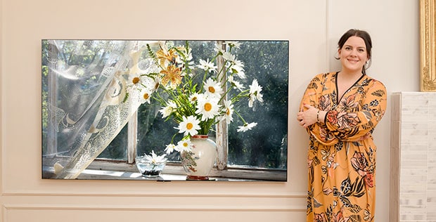 Frau steht neben Fernseher und lächelt