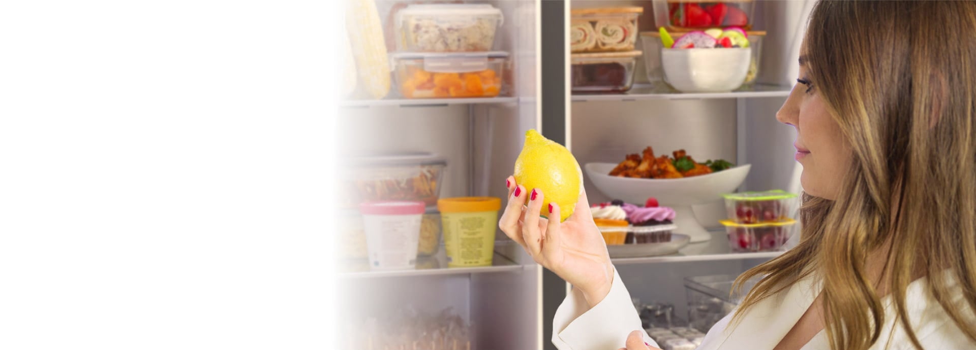 Eine Frau nimmt eine Zitrone vor der geöffneten Kühlschranktür des LG InstaVeiw Side-by-Side heraus.