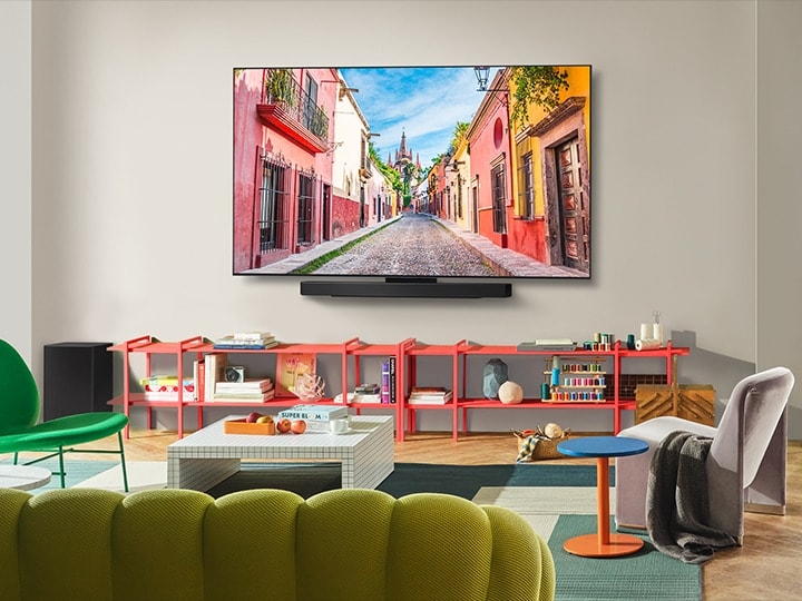 Frontalansicht des an der Wand montierten LG OLED-Fernsehers mit Soundbar in einem farbenfrohen Wohnzimmer, die das ultraschlanke Design und die perfekte Integration in den Raum verdeutlicht. 