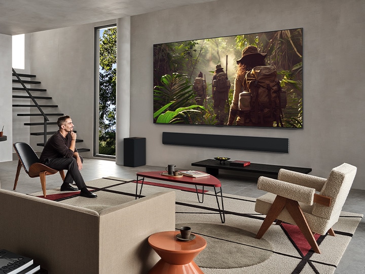 Weite Ansicht eines Wohnzimmers in einem hochwertigen Haus. Ein Paar sieht sich einen Film auf seinem an der Wand montierten LG OLED-Fernseher an. Das Design des Fernsehers fügt sich elegant in die Wand und die Inneneinrichtung ein.