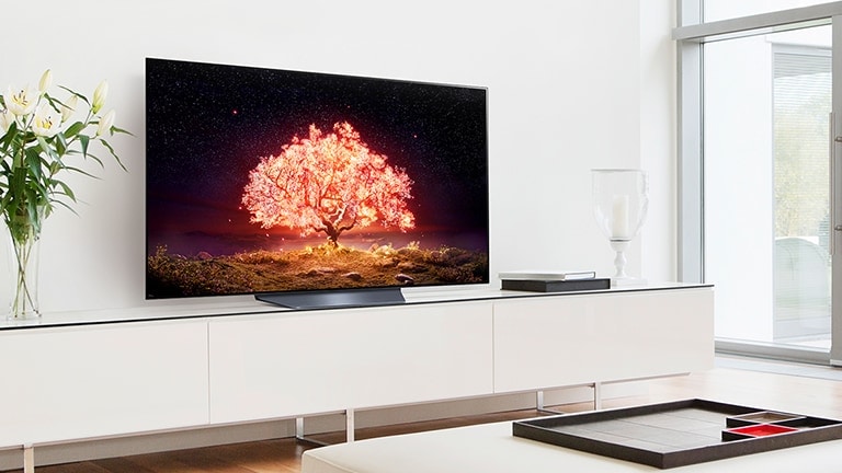 Ein Fernseher, der einen leuchtenden orangefarbenen Baum anzeigt, steht in einem Wohnzimmer mit weißer Einrichtung.