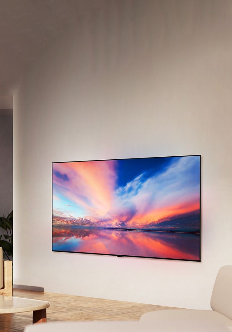 Der LG OLED TV B4 an der Wand eines neutralen Wohnraums, der ein buntes Foto eines Sonnenuntergangs über dem Meer zeigt. 	