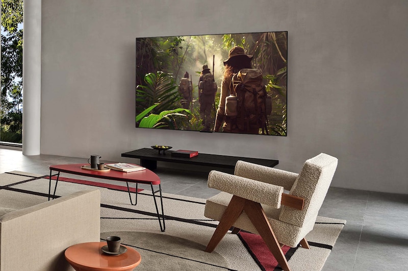 Bred visning af en stue i et luksushjem, hvor en mand ser en film på sit vægmonterede LG OLED TV. TV'ets design passer elegant til væggen og indretningen.