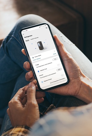 Billede, som viser en app, der gør det muligt at justere køleskabets indstillinger direkte fra en mobiltelefon, du holder i hånden.