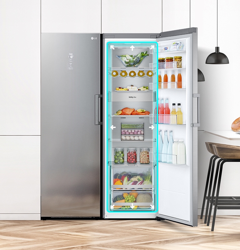 Køleskabet vist forfra i et køkken med døren åben og med produkterne indeni. En blå firkant fremhæver interiøret med pile, der peger ud for at indikere, at der er rigelig plads indeni.