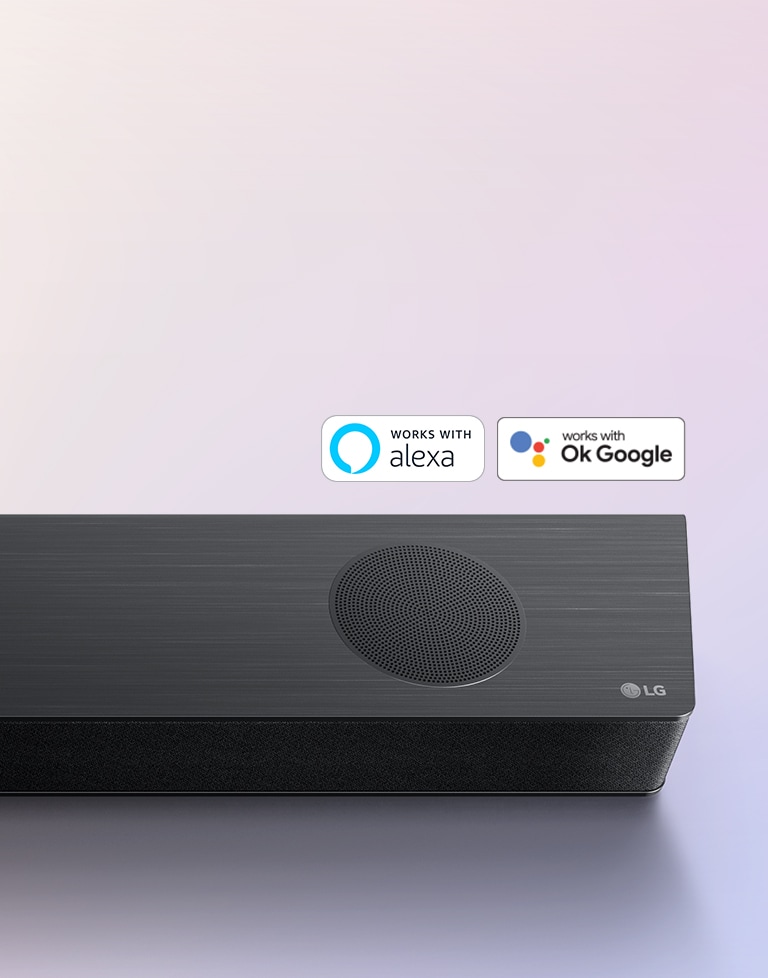 LG Soundbar er placeret på jorden og viser LG-logoet i højre hjørne af soundbaren. Alexa-logoet og OK GOOGLE-logoer er placeret på soundbaren.