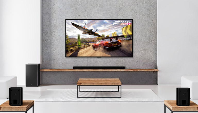 Et sæt med to baghøjtalere, en subwoofer, en soundbar og et tv i en hvid stue En kørende bil og et rumskib vises på tv-skærmen.