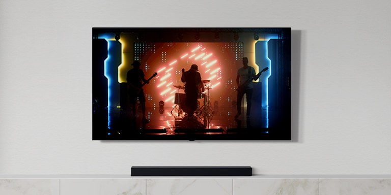 Der er et tv og en soundbar i den hvide stue. En gruppe, der spiller instrumenter og synger en sang på en tv-skærm. (afspil videoen)