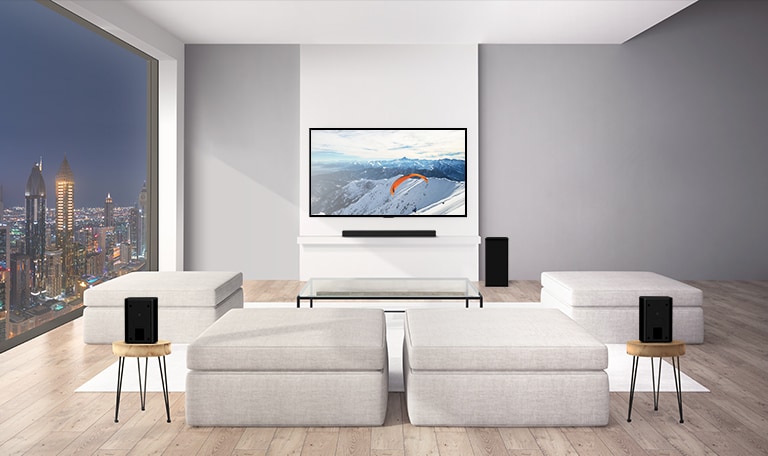 En LG Soundbar med en subwoofer og 2 baghøjttalere står i en stue. Grafik af lydbølger, der kommer ud fra baghøjttalerne til loftet og hopper tilbage. (afspil videoen)