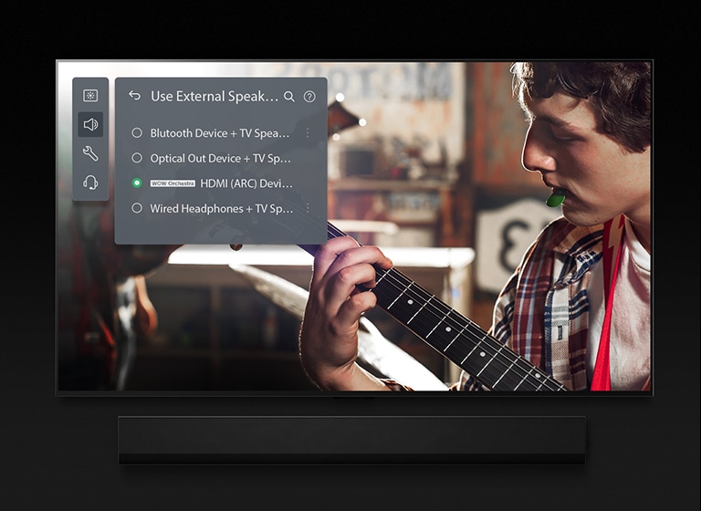 Et billede af et LG OLED TV med Soundbar. En video af en dreng, der spiller guitar, afspilles på skærmen med indstillingen for Soundbar ovenpå.