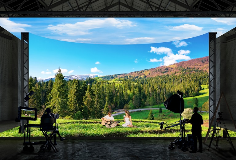 A virtual production studio with curved LED walls and ceiling and floor LEDs is filming images of a forest and field landscape.