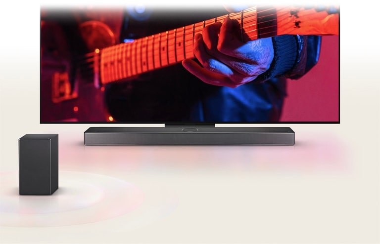 An LG TV displaying a man playing guitar and an LG Soundbar directly underneath, with another speaker in front.