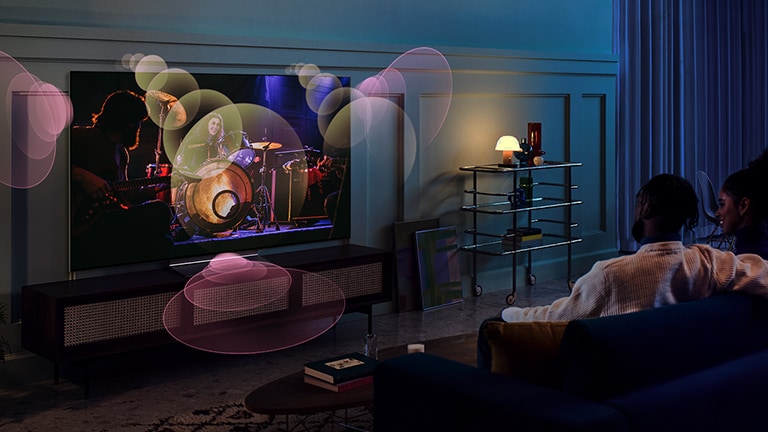 An image of an LG OLED TV in a blue, dimly lit room showing a music concert. Bubbles depicting virtual surround sound fill the space.