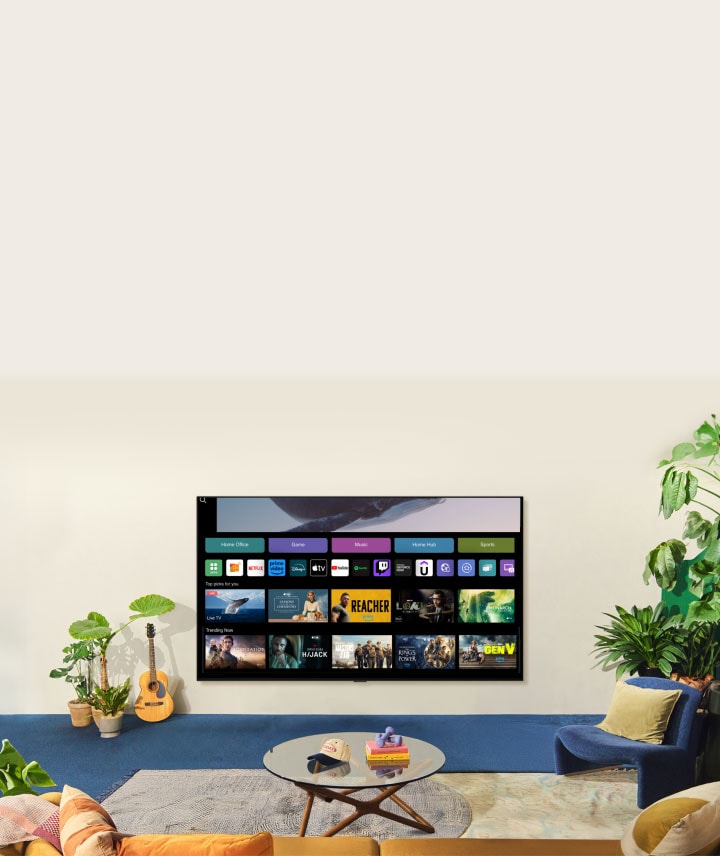 Se muestra una mujer nadando en el océano con ballena flotando encima. La pantalla de inicio aparece desde abajo. Mientras la escena cambia, se muestra un gran televisor LG TV en la pared. Dos mujeres están sentadas en un acogedor salón lleno de plantas y con una guitarra. Una mujer apunta con el mando a distancia a un televisor que muestra una variedad de aplicaciones y series recomendadas en la pantalla de inicio.